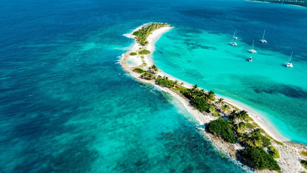 Île étroite et voiliers dans des eaux turquoise - photo d'illustration, monteur Girardin Inter Invest Outre-mer